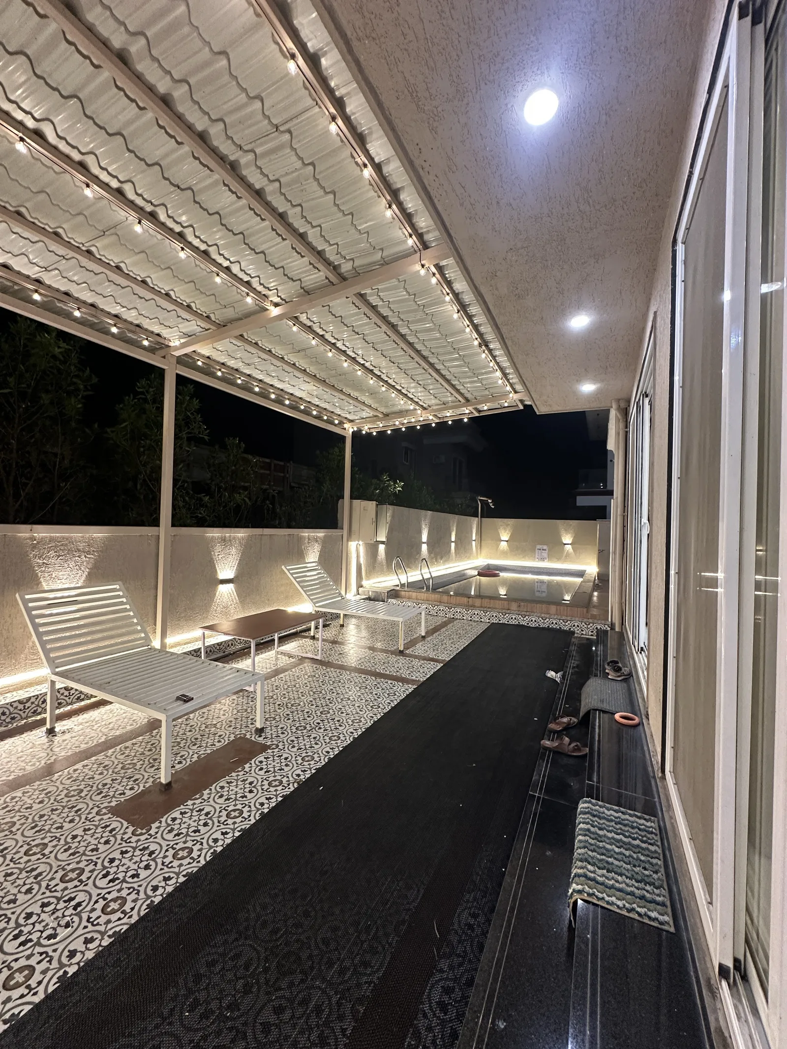 Aashiyana’s covered poolside passage with white loungers and string lights at night.