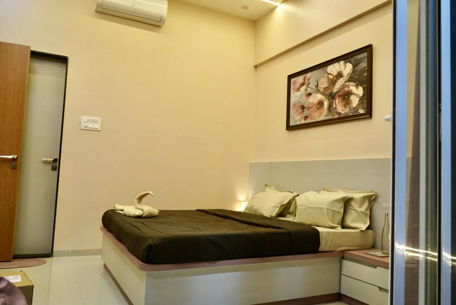 A bedroom with a made double bed, a towel swan and floral artwork above the headboard.