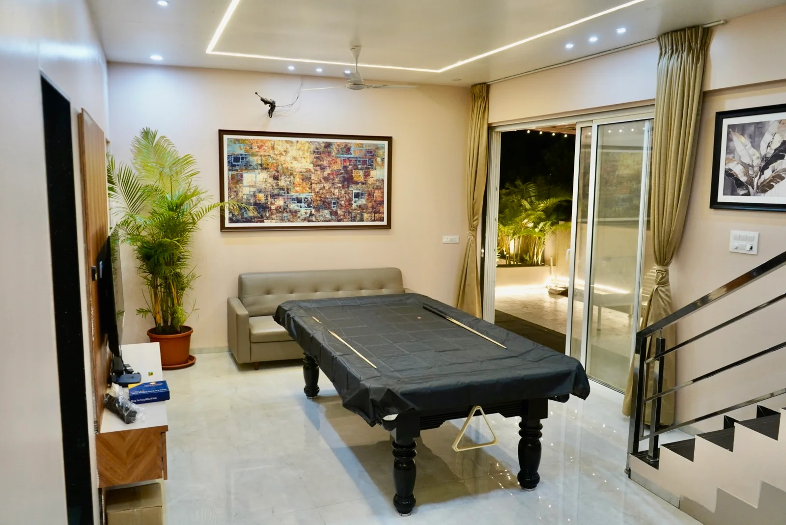 A covered pool table beside a sofa, television and sliding doors opening towards the deck.