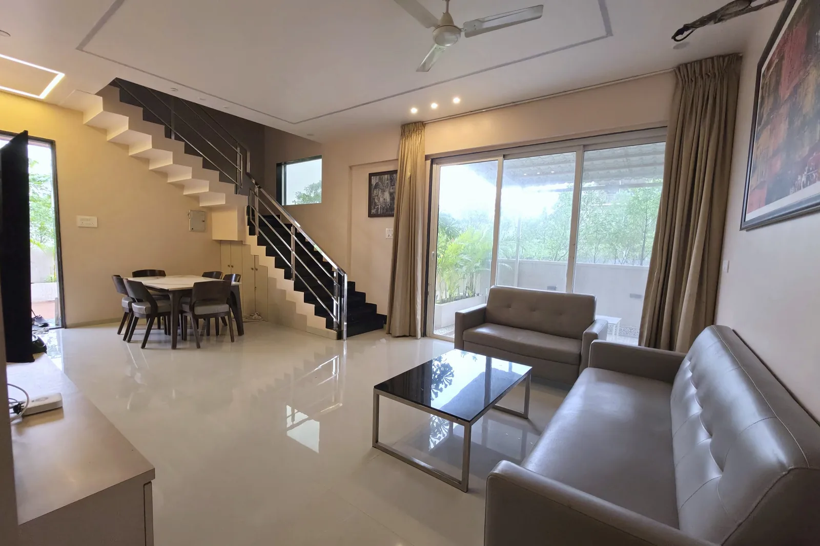 A living and dining room with sofas, a glass coffee table, dining chairs and a staircase.