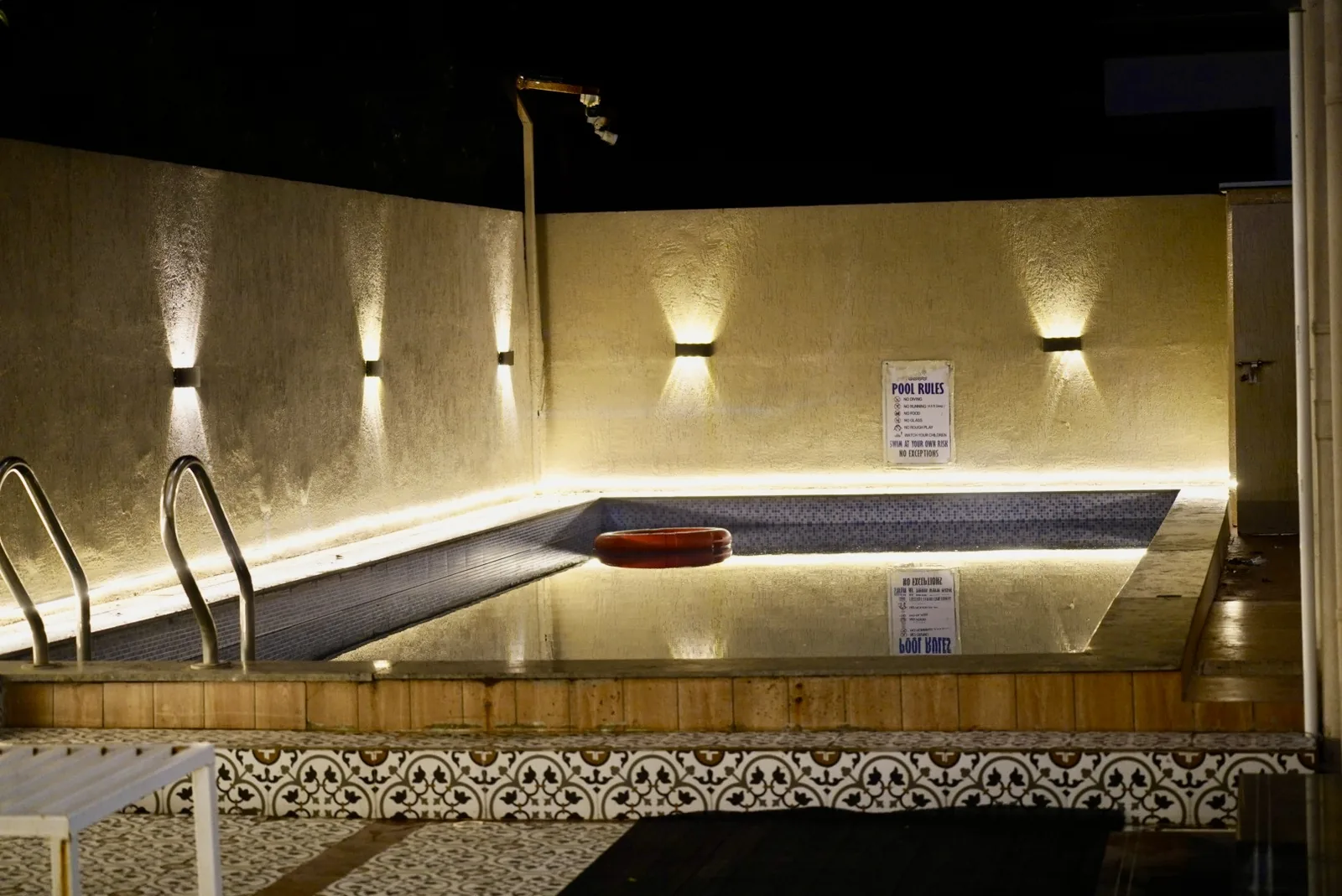 The outdoor pool at night, with wall lights and a metal pool ladder.